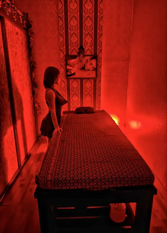 Empty massage bed in a red-lit room with patterned wallpaper at Ai Oon Massage Lanna