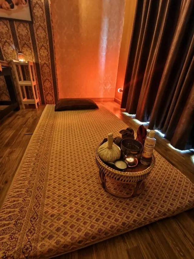 Floor mat with a basket of herbal compresses and oils in a candle-lit Thai massage room
