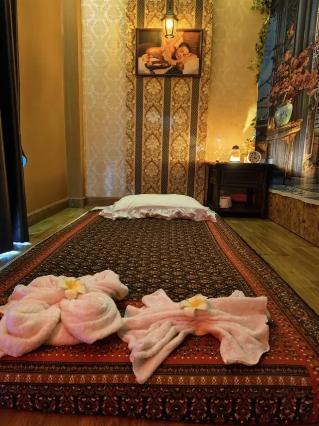 Thai massage floor mat with pink flower-shaped towels in a dim, warm room, Chiang Mai