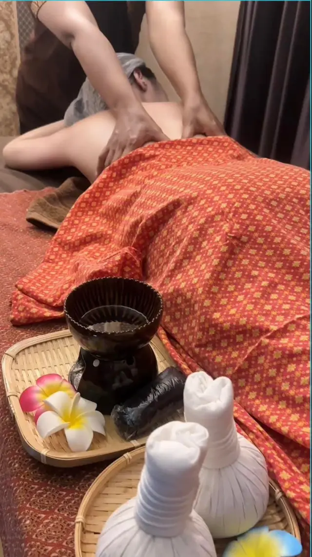 Herbal compress balls on a tray beside a guest receiving a back massage at Ai Oon Massage Lanna