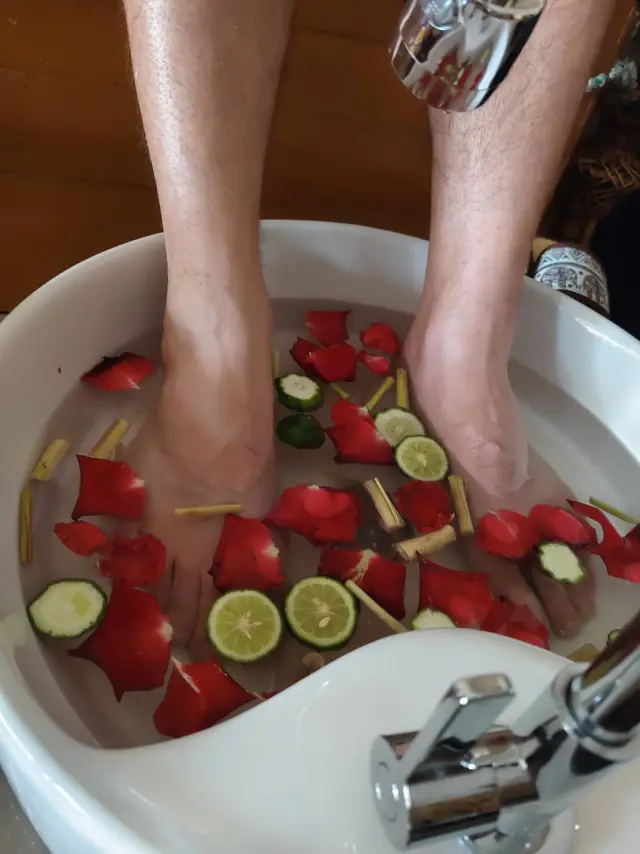 Feet soaking in a basin with red petals and lime slices before a foot massage in Chiang Mai