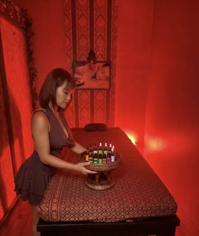 Therapist arranging a tray of massage oils on a bed in a red-lit room at Ai Oon Massage Lanna